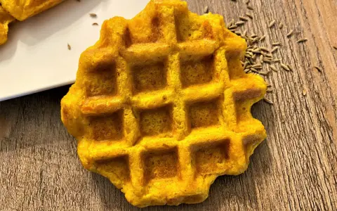Gaufre carotte dorée, parsemée de graines sur fond de bois. Un délice orangé à déguster.