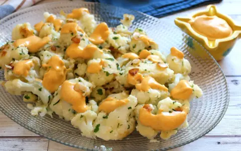 Coliflor al ajillo con salsa cremosa, adornada con perejil fresco y trocitos de ajo crujiente.