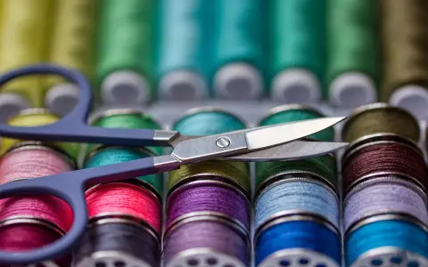 Ciseaux sur une rangée de bobines de fil à coudre aux couleurs vives. Le grosseur de fil à coudre varie, offrant un arc-en-ciel de possibilités créatives.