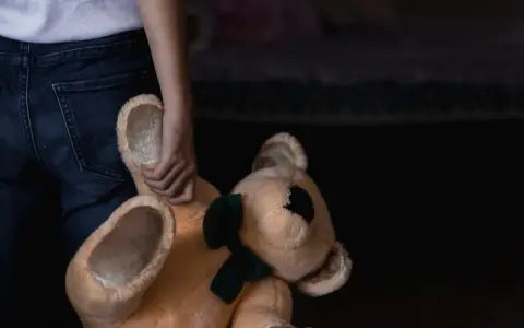 Main d'enfant tenant un ours en peluche. Un signalement enfance en danger en ligne peut aider.