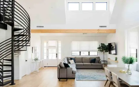 Ampio soggiorno con scala a chiocciola nera, divano angolare grigio e trave in legno a vista. Loft idee originali per un ambiente moderno.