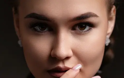 Gros plan sur un visage féminin aux **sourcils droits** et maquillés. Elle porte des boucles d'oreilles discrètes.