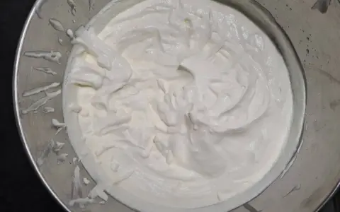 Crème fouettée onctueuse dans un bol en métal, prête à garnir un délicieux gâteau.