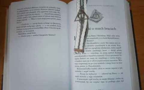 Otwarta książka z zakładką w kształcie symbolu Insygniów Śmierci. Tekst opowiada baśń o trzech braciach.