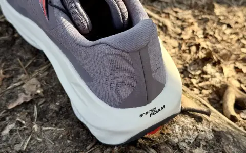 Szary but Salomon Ultra Glide 3 z białą podeszwą i napisem "energy FOAM" na tle leśnej ściółki.