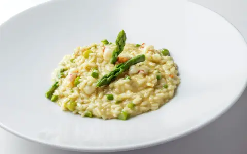 Risotto cremoso con asparagi freschi e succulenti gamberetti, guarnito con punte di asparagi croccanti.