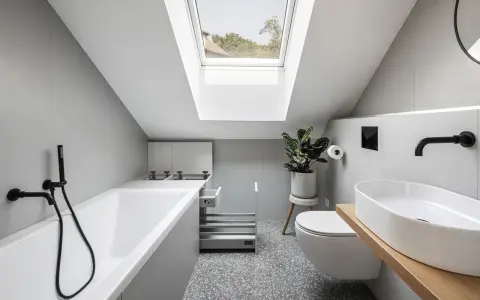 Un piccolo bagno sottotetto basso con vasca, WC, lavabo e lucernario.