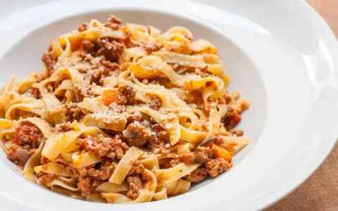 Tagliatelle z bogatym, mięsnym sosem bolońskim, posypane parmezanem. Pyszne danie, które zadowoli każdego miłośnika włoskiej kuchni.