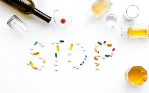 Nalewki, kieliszki i tabletki tworzą napis STOP. Różne rodzaje alkoholizmu i leczenia.