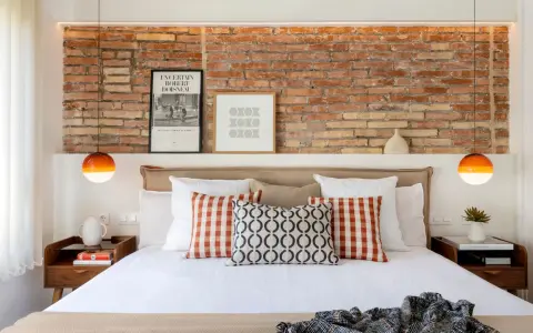 Ideas para decorar la pared de la cabecera de la cama: ladrillo visto, cuadros y lámparas naranjas.