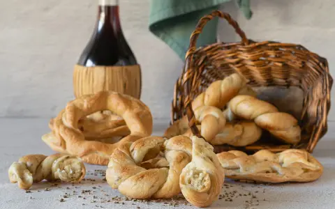 Pane intrecciato e ciambelle, ispirazione per ricette ciociare, accanto a una bottiglia di vino rosso e un cesto di vimini.