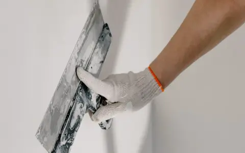 Mano enguantada alisando masilla para tapar agujeros en la pared.