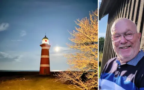 Rött och vitt fyr på Gotland i månsken, bredvid ett träd med gyllene löv. Till höger en glad man med glasögon.