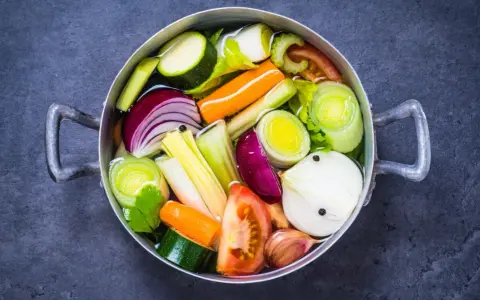 Olla con verduras cortadas en trozos: cebolla, zanahoria, calabacín, puerro, tomate y ajo.