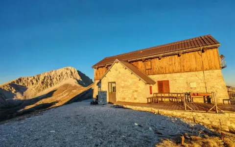 Il rifugio Duca degli Abruzzi, con la sua struttura in pietra e legno, si erge maestoso al tramonto, dominando un paesaggio montano aspro e solitario.