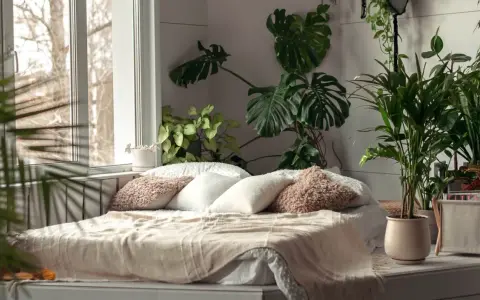 Sypialnia z bujną roślinnością, gdzie różnica między stylem tropikalnym a "urban jungle" w aranżacji wnętrz jest subtelna. Duże liście monstery i palmy tworzą zieloną oazę.
