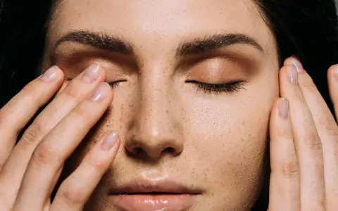 Primo piano di una donna con lentiggini, che si tocca il viso. Potrebbe indicare sintomi di carenza vitamina d sulla pelle.