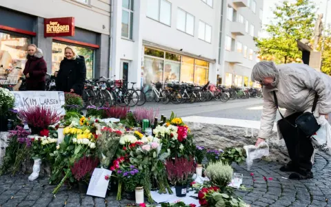 En kvinna lägger blommor vid en minnesplats för Kim Larsen. Många blommor och ljus.