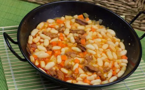 Alubias con chorizo y verduras en una paellera, plato tradicional español.