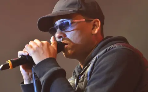 Mann mit Kappe und Sonnenbrille singt ins Mikrofon. Ein starker musik comeback Moment.