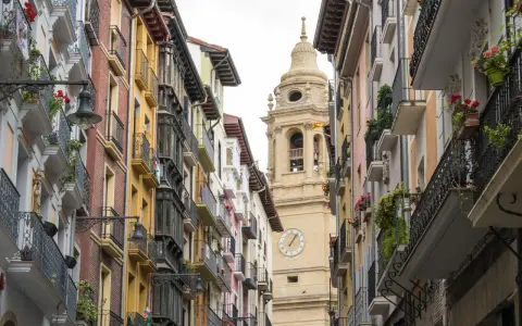 Edificio con balcónes floridos y torre de iglesia en Navarra. ¿Buscas ayudas cambio ventanas Navarra?