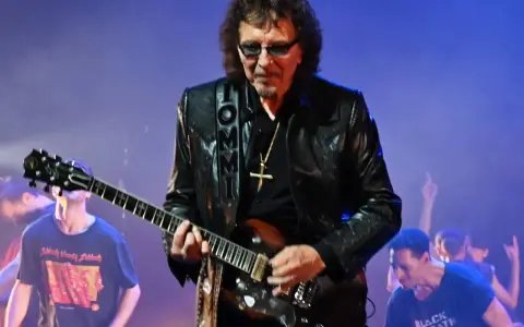 Tony Iommi, Gitarrist von Black Sabbath, spielt auf der Bühne. Im Hintergrund jubelt das Publikum.