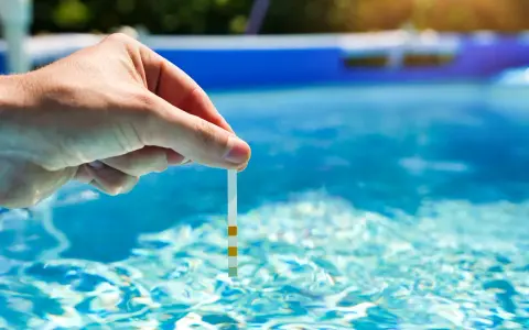 Main tenue une bandelette de test dans l'eau d'une piscine pour vérifier la qualité de l'eau, essentielle au bon fonctionnement du système pompe piscine.