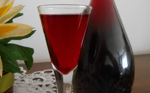 Szklanka z nalewką z aronii mrożonej na wódce, obok ciemna butelka. W tle ozdobny kwiat.