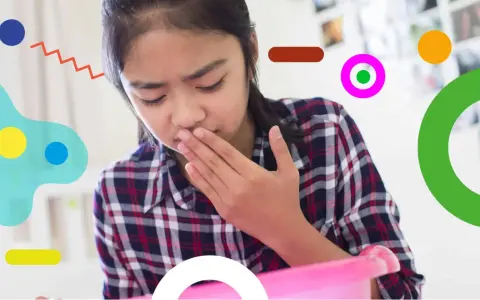 Bambina con nausea, forse per farmaci, copre la bocca con la mano, pronta a vomitare in un contenitore rosa.