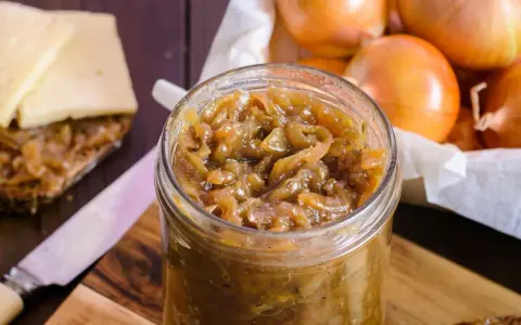 Słoik pełen aromatycznej, karmelizowanej cebuli, idealnej na kanapkę z serem. Obok leżą świeże cebule.
