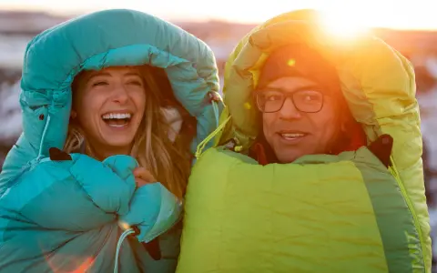 Glückliches Paar in Schlafsäcken bei Sonnenuntergang. Die Frage welcher Schlafsack bei welcher Temperatur ist hier wohl gelöst!