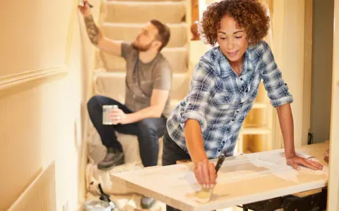 Pareja renovando su hogar con una reforma sin obras. Ella pinta una puerta, él la pared.