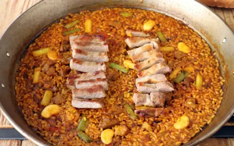 Arroz con secreto, un plato de paella con cerdo tierno y verduras crujientes, listo para ser disfrutado.