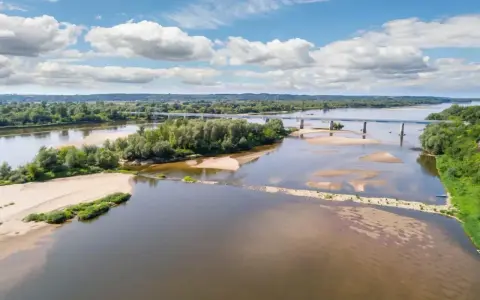 Szeroka rzeka z piaszczystymi łachami i zielonymi wyspami, przecinana mostem. To krajobraz Wisły, najgłębszej rzeki w Polsce, w słoneczny dzień.