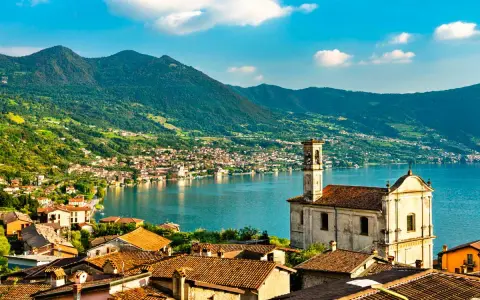 Un borgo pittoresco sul lago, ideale per gite in giornata da Milano. Case con tetti rossi, una chiesa e montagne verdi sullo sfondo.