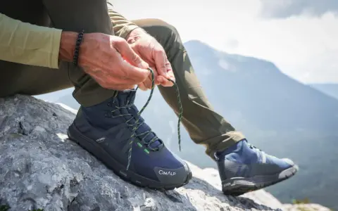 Uomo lega i lacci di scarponi da hiking su roccia, pronto per il trekking in montagna.
