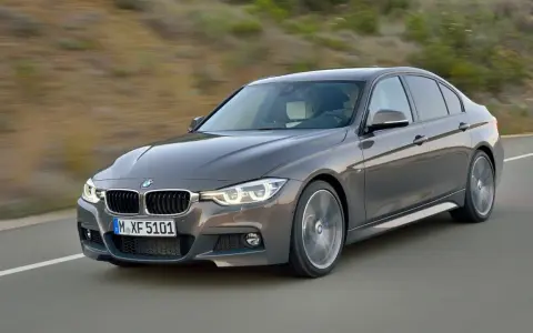 Szary sedan BMW F30 z dynamicznymi silnikami pędzi po drodze, ukazując sportowy charakter.