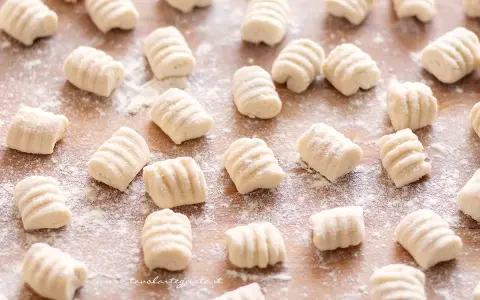 Gnocchi di ricotta freschi, pronti per essere cucinati, spolverati di farina su un tagliere di legno.