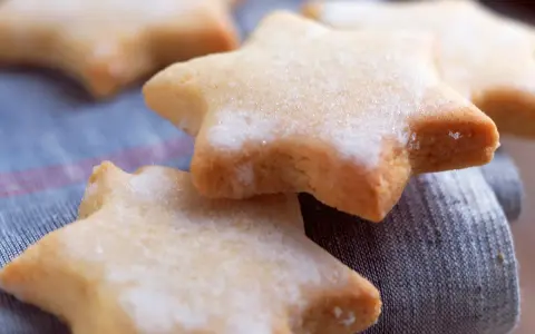 Des sablés au citron en forme d'étoiles, saupoudrés de sucre, reposent sur un tissu bleu.