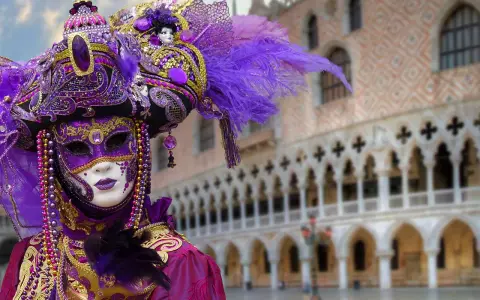 Un elaborato costume di Carnevale a Venezia, uno dei carnevali famosi in Italia, con maschera viola e oro, piume e perline.