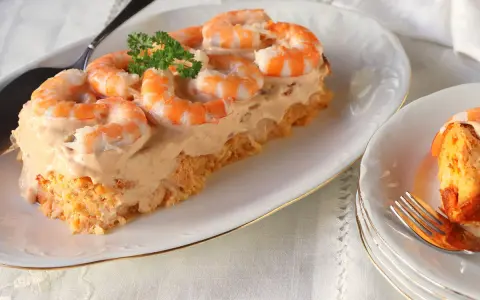 Delicioso pudin de pescado cubierto con crema y camarones, decorado con perejil.