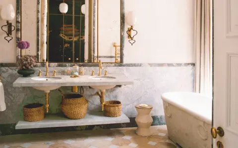 Elegante baño con doble lavabo de mármol, bañera exenta y suelo de baldosas. Un espejo con marco dorado y un cuadro oriental añaden un toque de lujo. ¡Ideas para pintar azulejos baño!