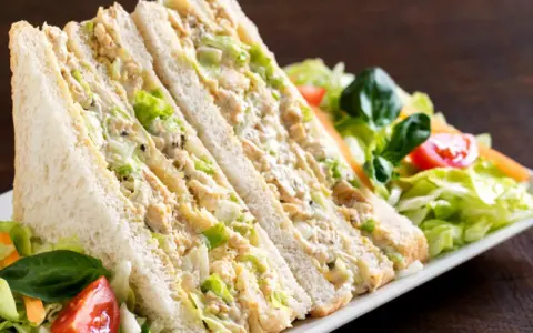Sándwich de pollo cortado en triángulos, relleno de pollo desmenuzado y lechuga, acompañado de ensalada fresca.