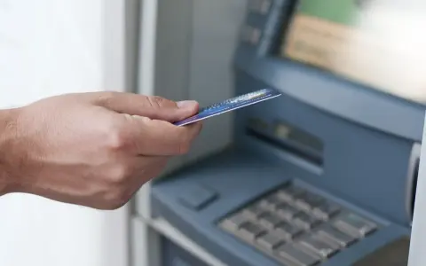 Dłoń z kartą zbliża się do bankomatu. Może to być związane z obsługą konta w Credit Agricole, a nie z zajęciami komorniczymi.
