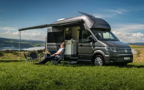 Mężczyzna odpoczywa przy kamperze VW California. Wymiary tego pojazdu pozwalają na komfortowe podróżowanie i biwakowanie.