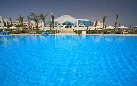Basen w Hilton Marsa Alam Nubian Resort. Wiele osób odpoczywa na leżakach pod palmami.