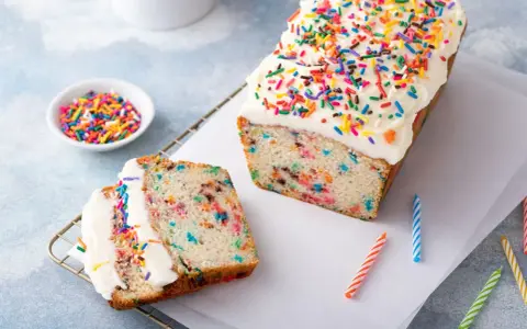 Bunter Konfetti Kuchen mit weißer Glasur und Streuseln. Ein Stück ist angeschnitten und zeigt die bunten Sprenkel im Teig.