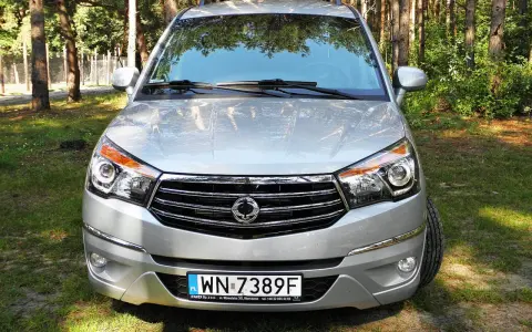 Srebrny SsangYong Rodius z przodu, zaparkowany na tle lasu.
