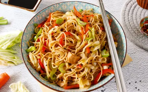 Un plato de chow mein con verduras coloridas y palillos listos para disfrutar.