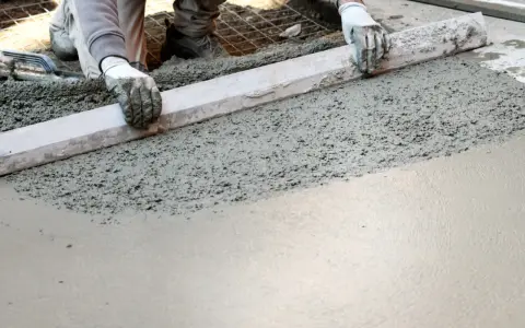 Ręce w rękawiczkach wyrównują świeży beton na taras za pomocą łaty.